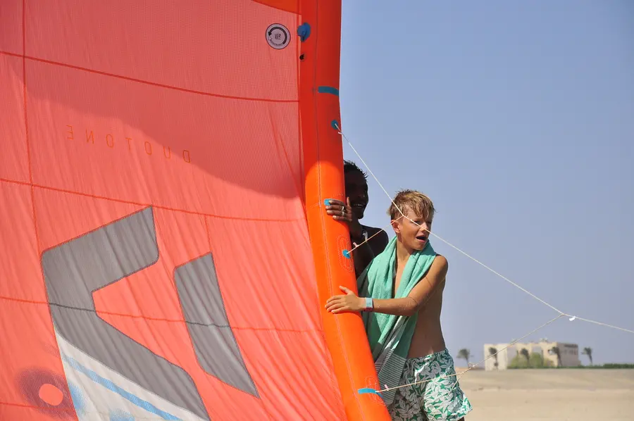 Young student and instructor steadying a large orange kite on the beach during a lesson at KiteMood