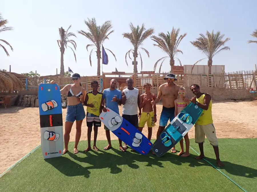 Group of instructors, adults and children holding kiteboards on the green lawn at the KiteMood base
