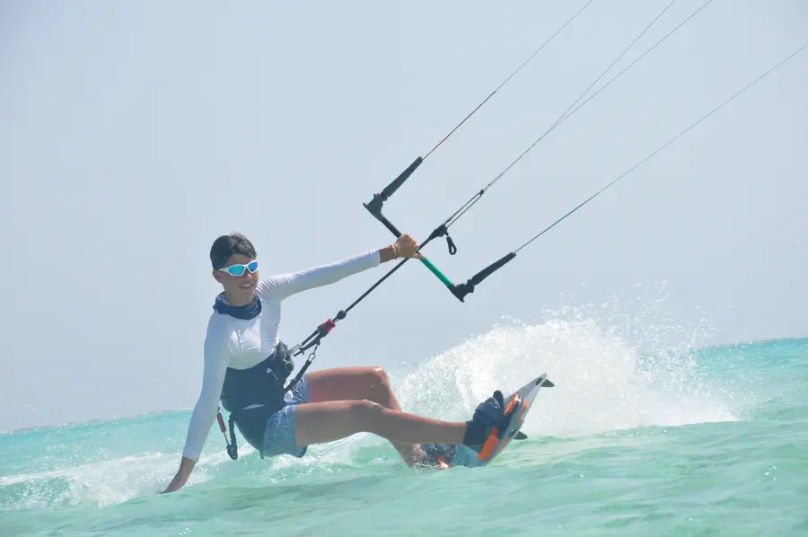 Rider in a white long-sleeved top carving a turn on turquoise water with spray flying behind the board