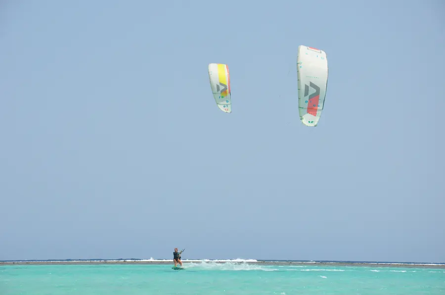 Two kites flying high above the turquoise lagoon at KiteMood Marsa Alam, with a kitesurfer riding far below